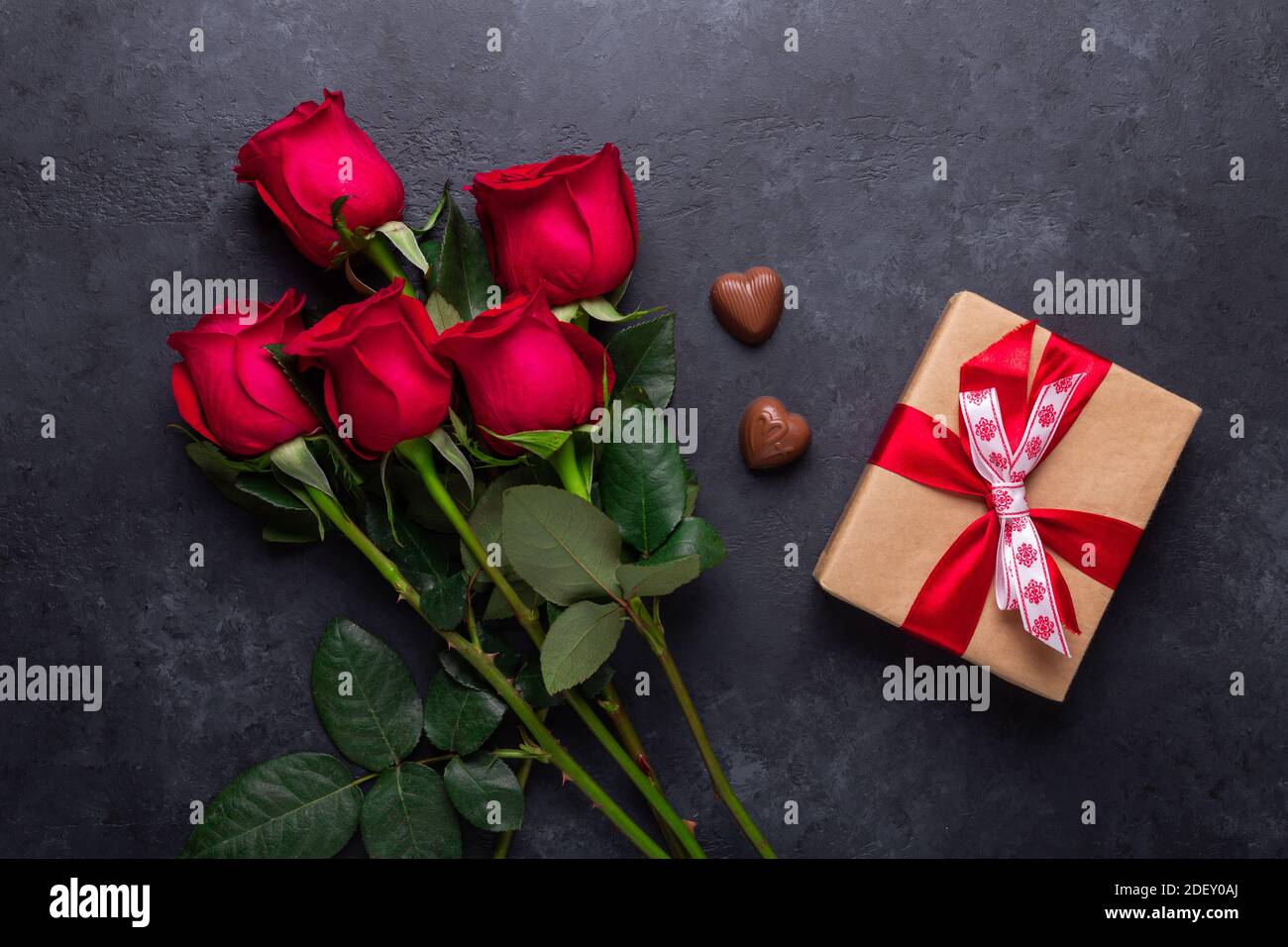 Flores de color rosa roja ramo, caja de regalo, dulces de chocolate sobre  piedra negra fondo día de San Valentín tarjeta de felicitación espacio de  copia Lay plano Fotografía de stock -