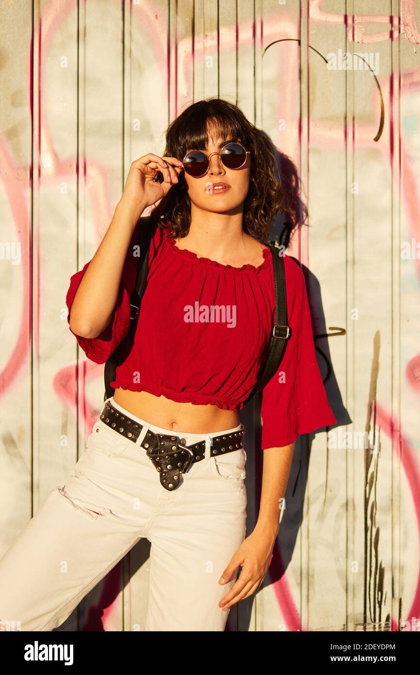 Foto de una adolescente de pie delante de una pared llena de graffiti. Ella  está usando un paño informal y gafas de sol Fotografía de stock - Alamy