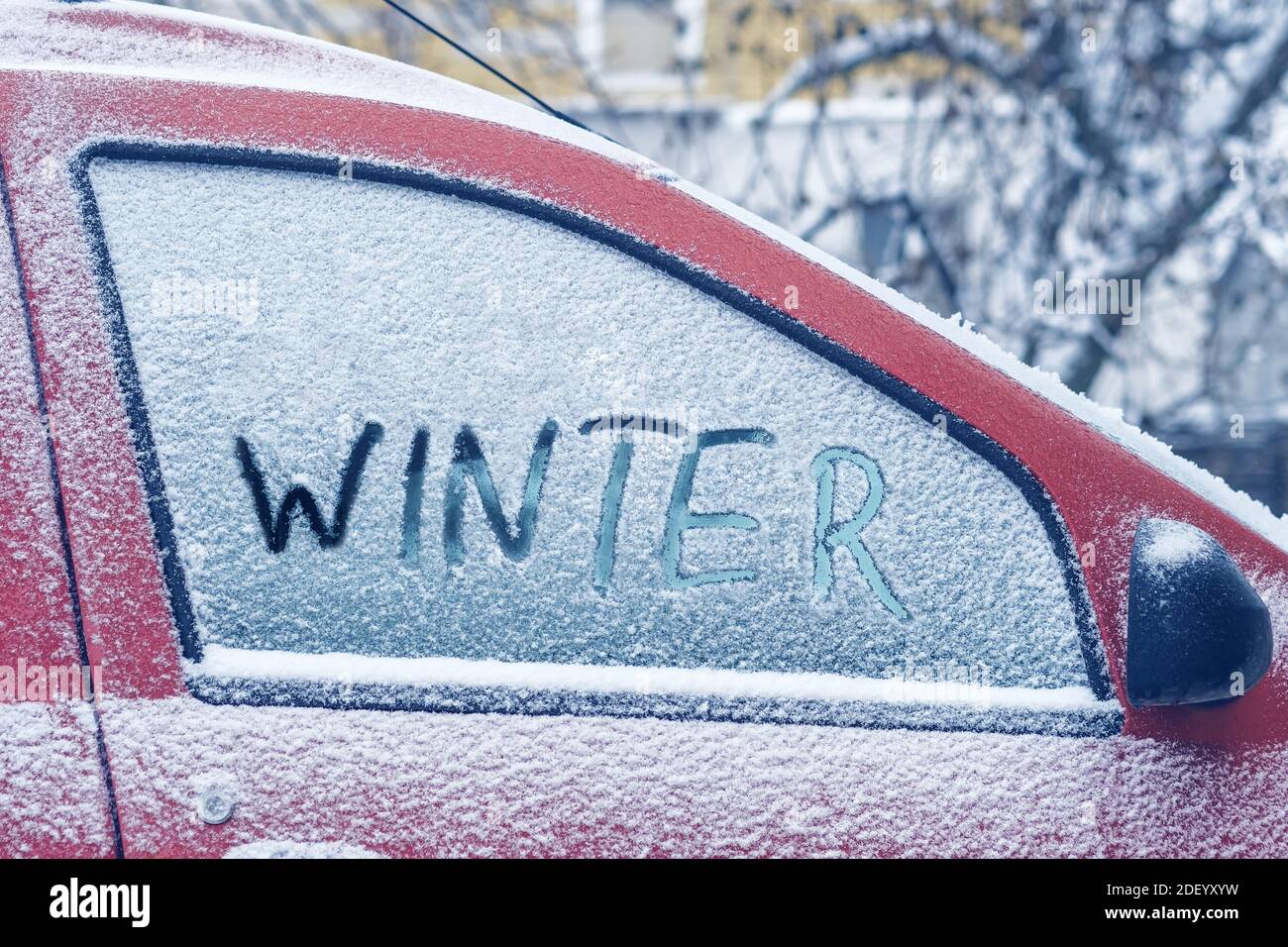 Word Winter escrito con el dedo en una ventana de nieve de un coche rojo Foto de stock