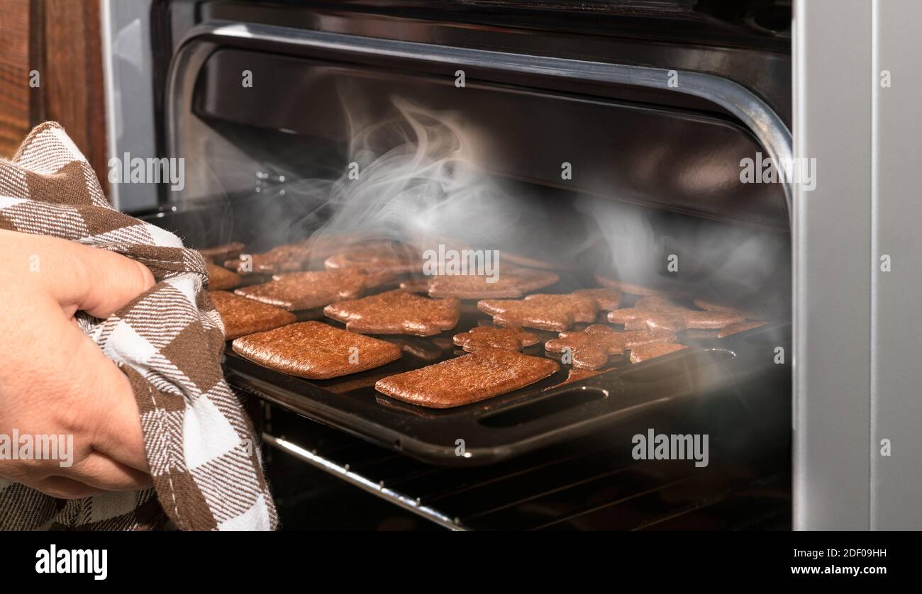Sacar a mano galletas de pan de jengibre de Navidad del horno de cocina al  vapor abierto. Preparación tradicional de Navidad y año Nuevo. Pastel  caliente ligeramente quemado Fotografía de stock -