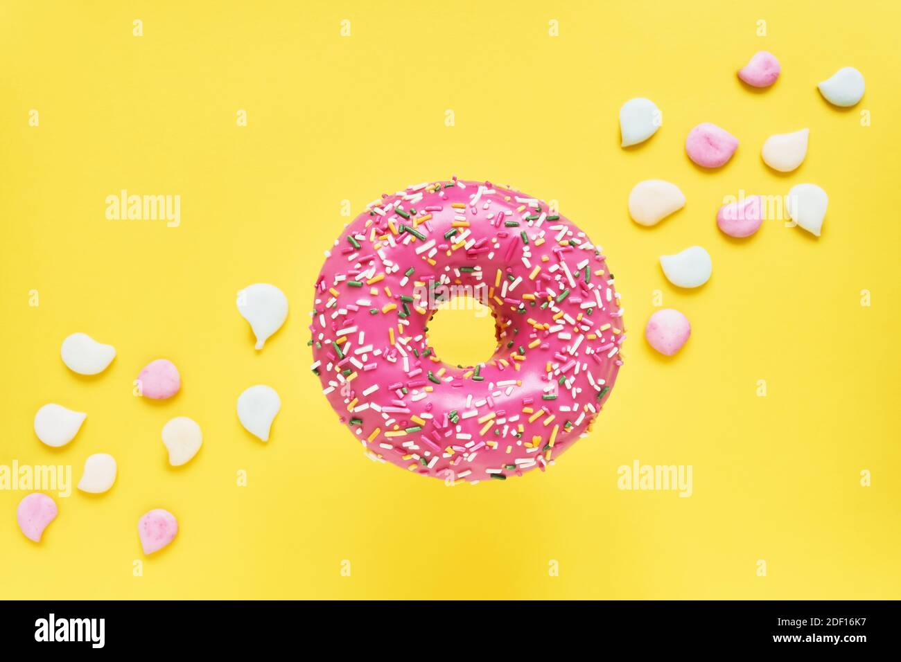Rosada rosada. Donut vidriado sobre fondo amarillo brillante con caramelos coloridos. Vista superior, espacio de copia Foto de stock