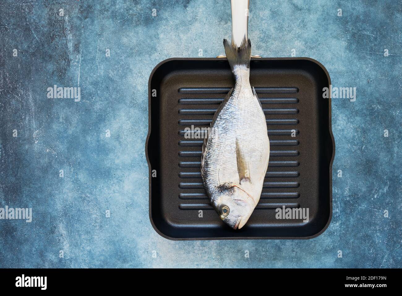 Dorado fresco o pescado de besugo en sartén sobre fondo azul. Vista superior, espacio de copia. Foto de stock