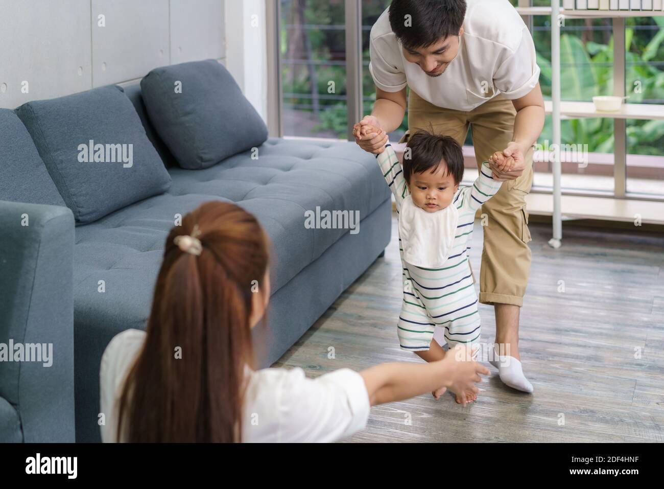 Bebé hijo asiático dando los primeros pasos adelante a su madre. Bebé feliz aprendiendo a caminar con el padre ayuda y enseñando cómo caminar gentileza ho Foto de stock
