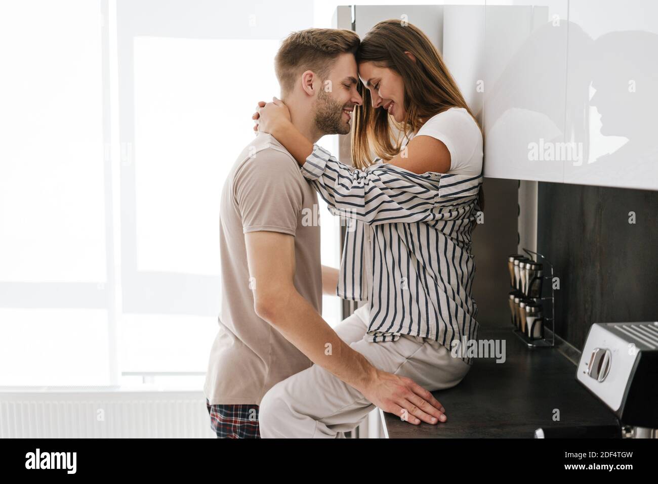 Joven hermosa pareja caucásica en ropa de ocio sonriendo y abrazando juntos en casa Foto de stock