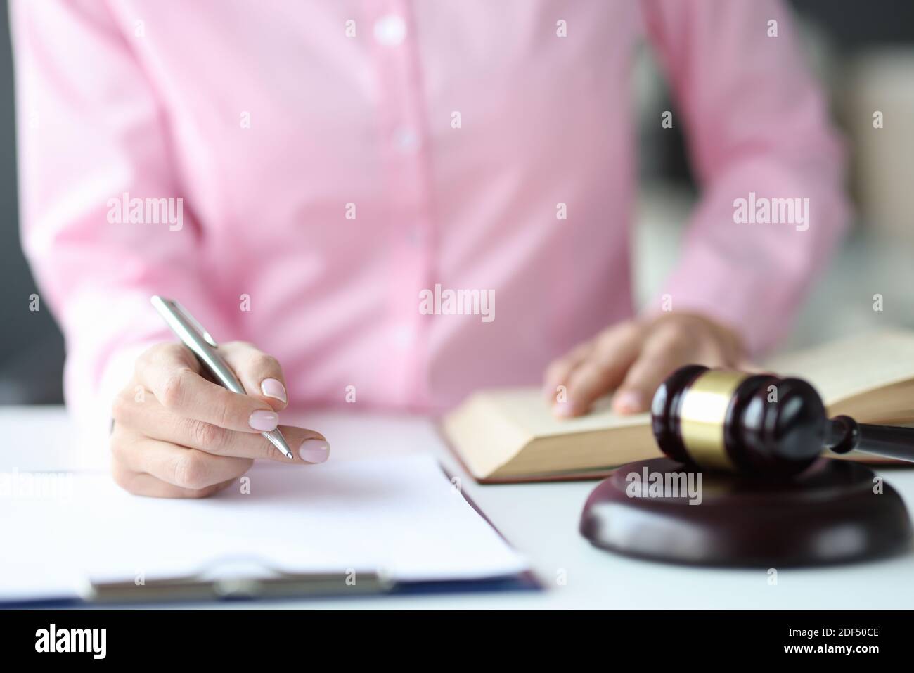 Mujer juez escribiendo en documentos con bolígrafo cerca de martillo de la corte Foto de stock