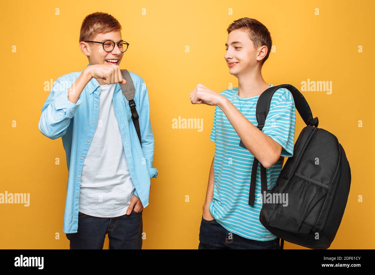 Dos adolescentes con estilo, chicos se saludan unos a otros, sobre un fondo amarillo Foto de stock