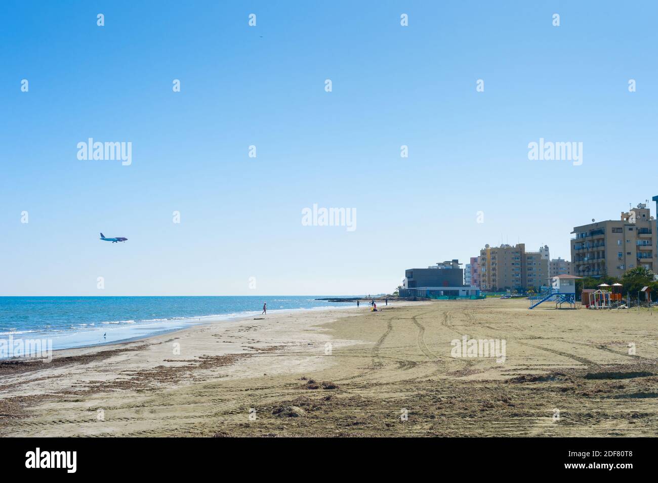 El avión llega al aeropuerto de Larnaca. Playa de arena y edificio de apartamentos. Larnaca, Chipre Foto de stock