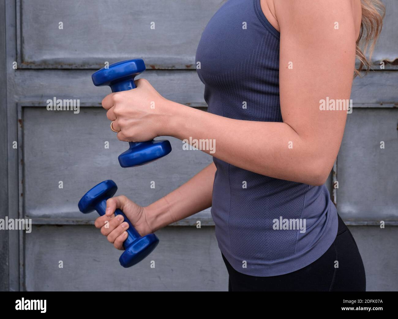 el cuerpo de la mujer joven hace bíceps con mancuernas azules