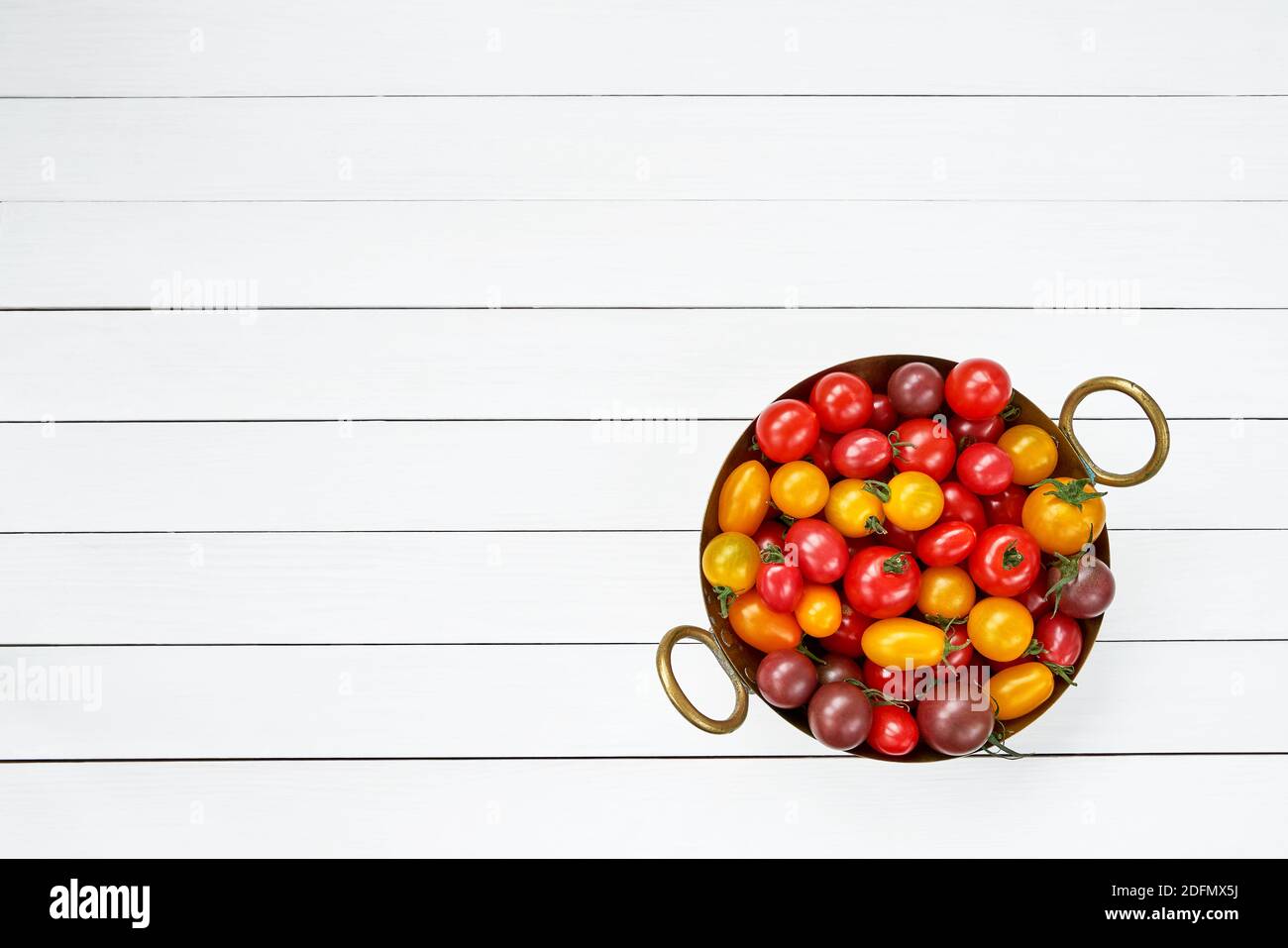 Tomates de colores en colander sobre mesa de madera blanca. Vista superior, espacio de copia Foto de stock