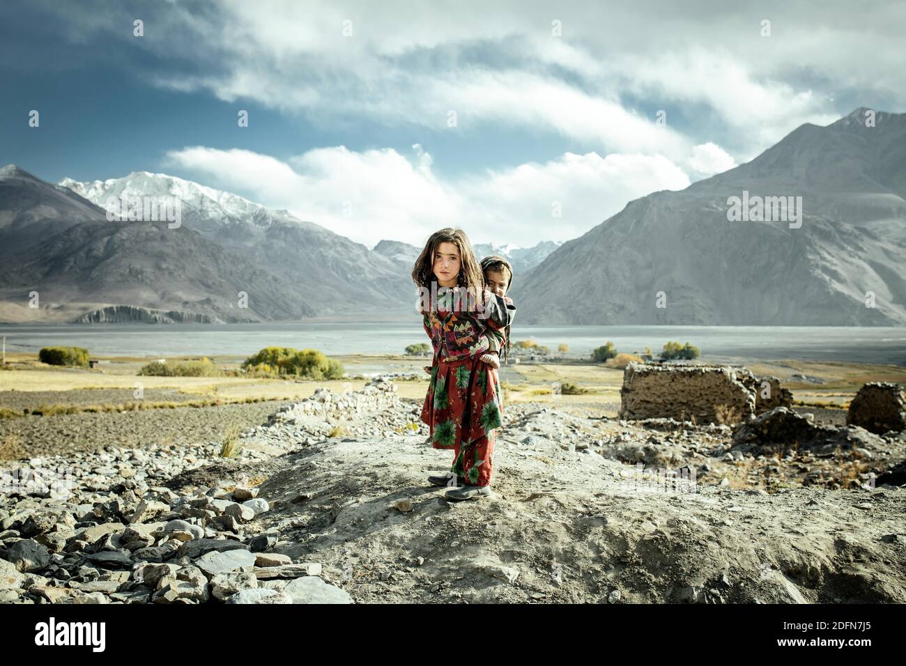Niña que lleva a su hermano pequeño en la espalda, miembros del grupo étnico sedentario Wakhi, Saradh-e-Broghil, Corredor Wakhan, Afganistán Foto de stock