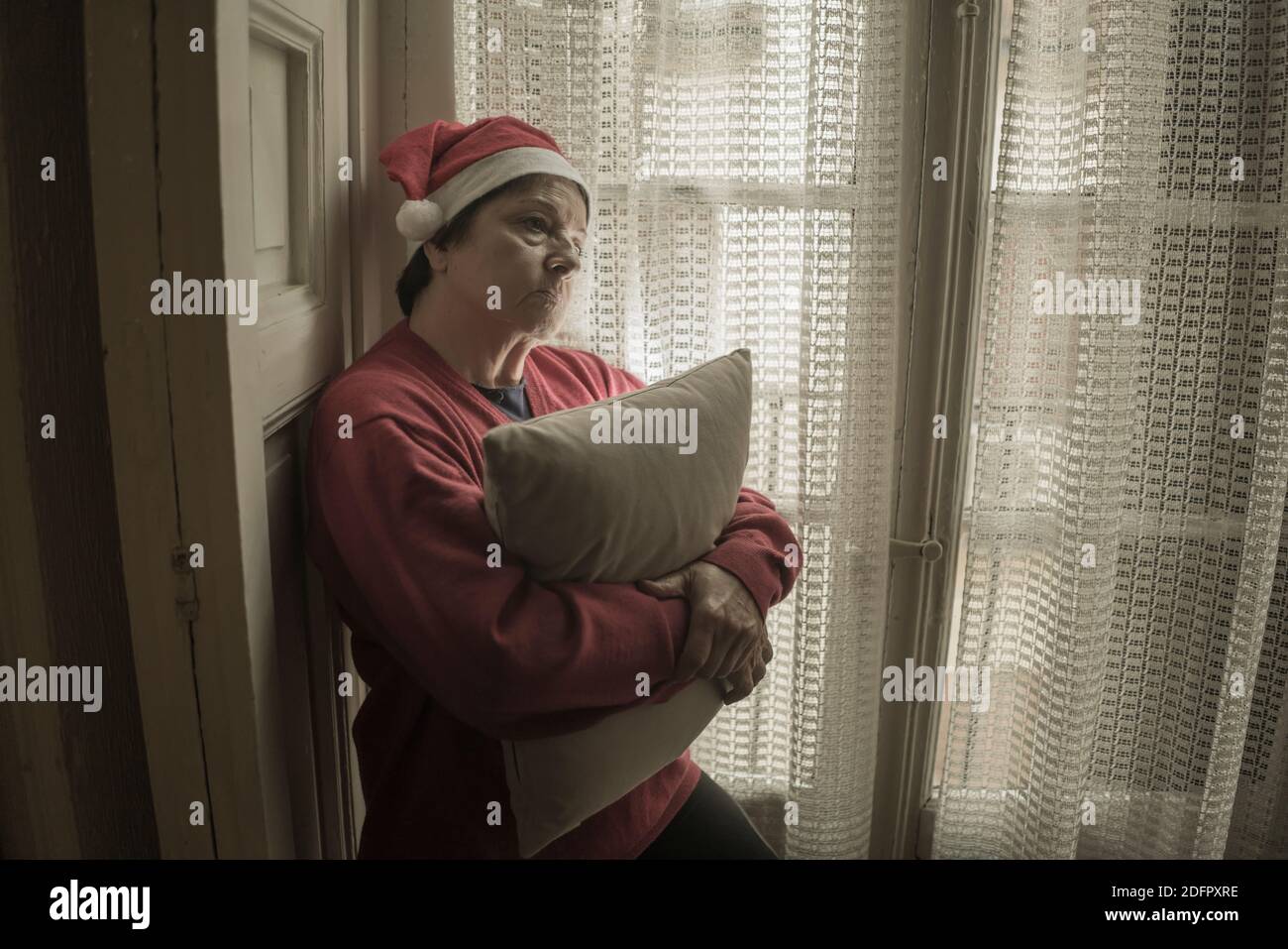 Mujer mayor teniendo triste Navidad solo - mujer jubilada madura 60 o 70 años en el sombrero de Santa Claus deprimido y emocional en casa sintiéndose solo y melanca Foto de stock