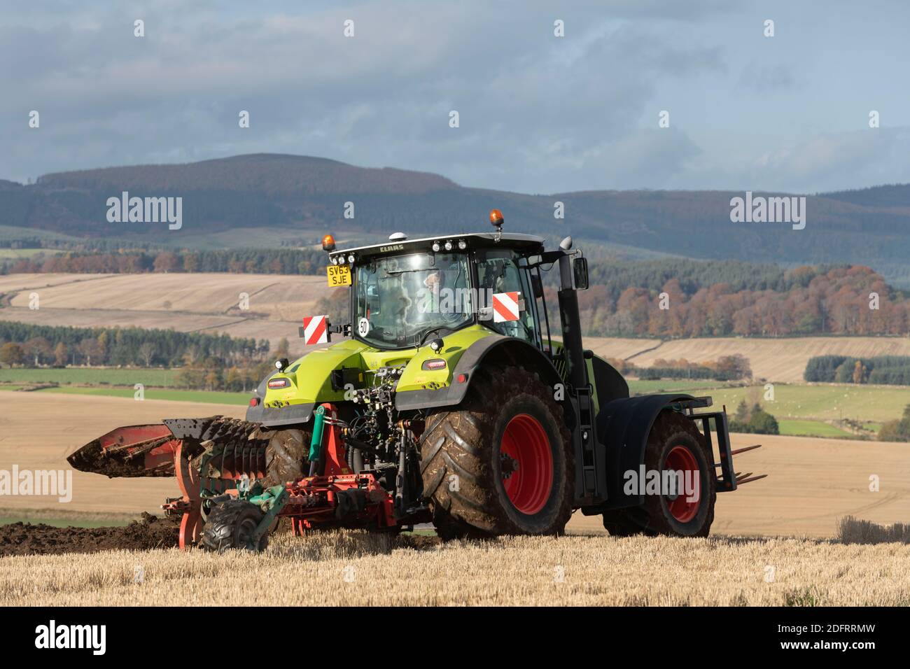 Un tractor Claas Axion 940 y un arado reversible Kverneland Variomat Trabajando en tierras de cultivo en Aberdeenshire con Menaway Hills in La distancia Foto de stock