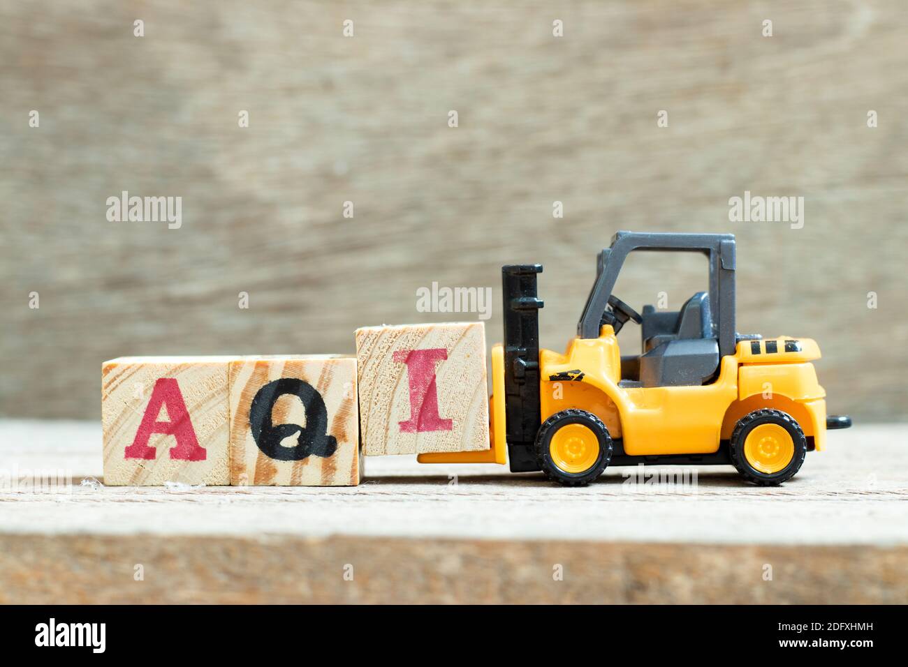Carretilla elevadora de juguete mantener la letra bloque I para completar la palabra AQI (Índice de calidad del aire) sobre fondo de madera Foto de stock