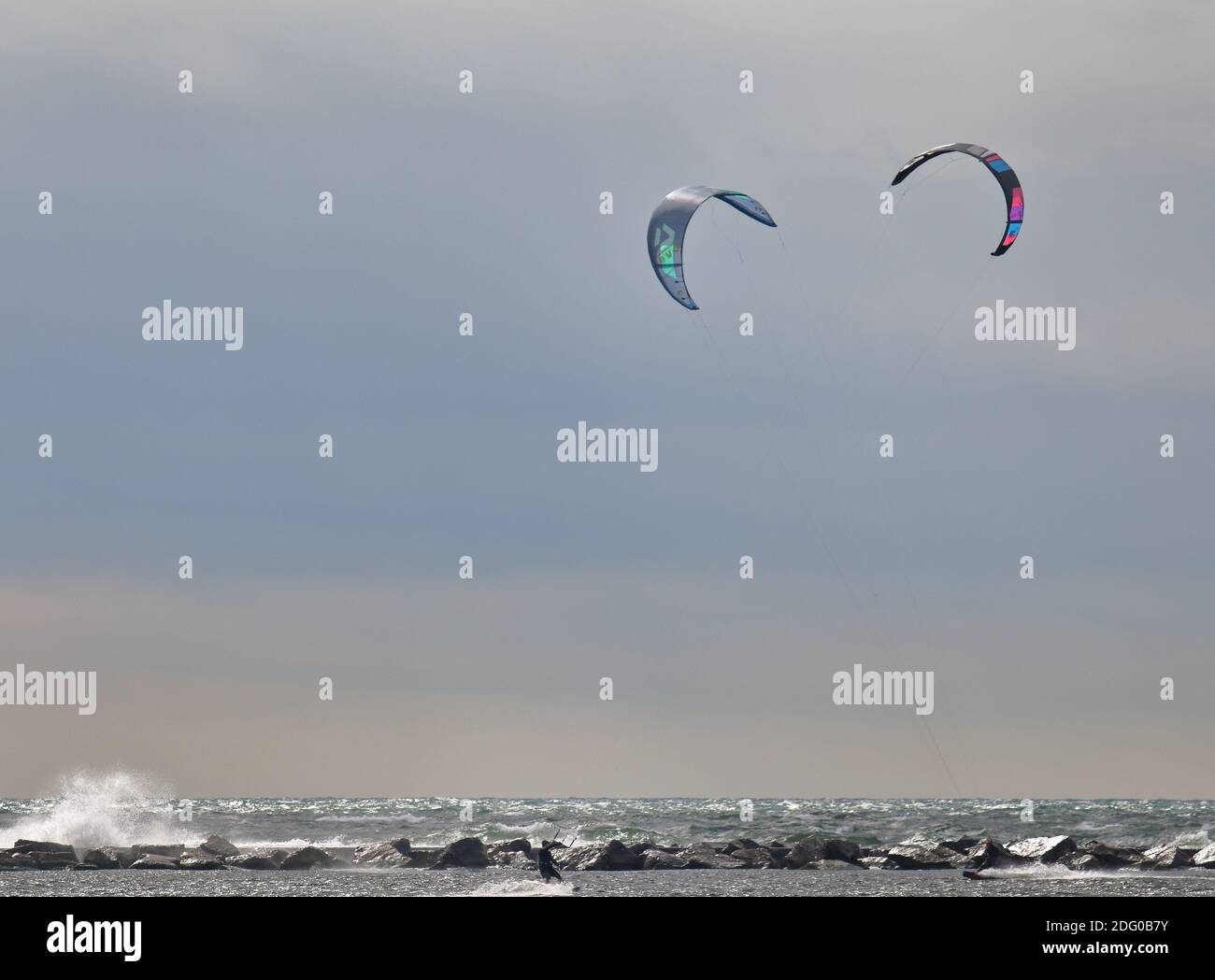 Dos kite-boarders windsurf en un día nublado con una roca embarcadero en el fondo Foto de stock