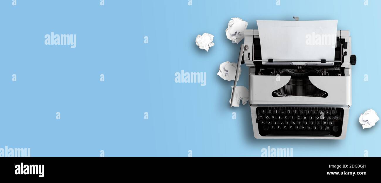 vista superior de la vieja máquina de escribir y bolas de papel arrugadas sobre fondo de escritorio azul, escritura o concepto de blogs Foto de stock