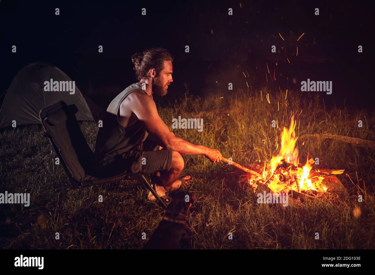 Hombre acampando al aire libre por la noche sentado junto a una hoguera Foto de stock