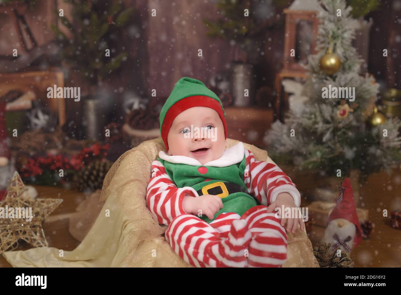 Feliz bebé elfo ayudante de Santa en traje Santa Claus con regalo en el  árbol de Navidad Fotografía de stock - Alamy