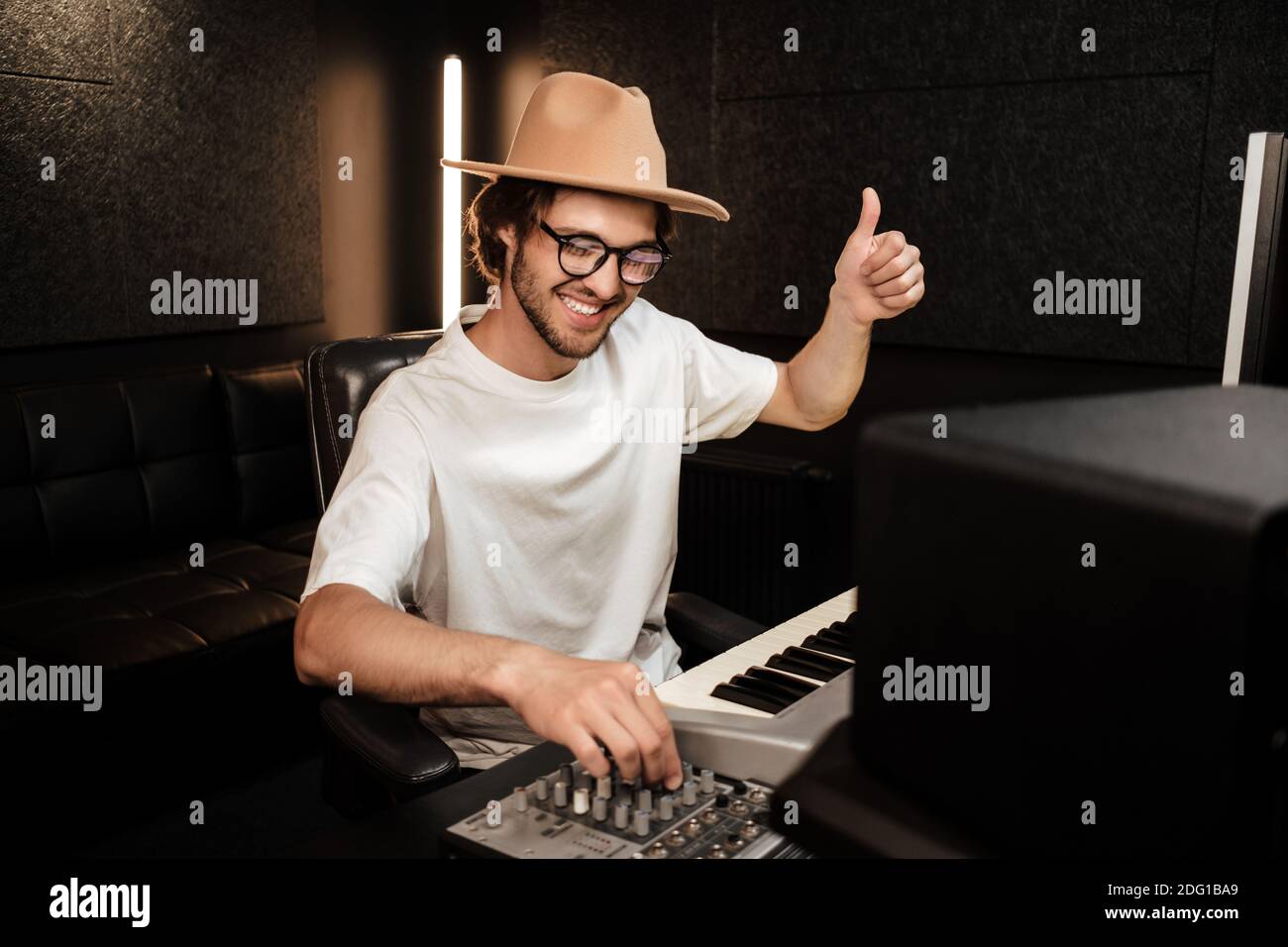 Joven productor de música con estilo mostrando feliz pulgar arriba gesto componer nueva canción en estudio de grabación de sonido. Como gesto Foto de stock