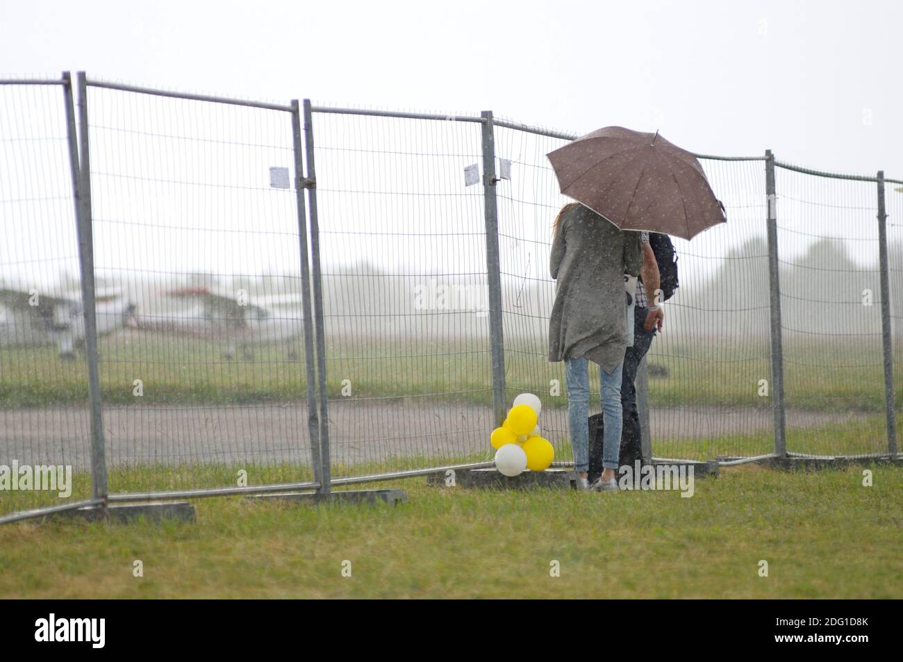 Bajo la lluvia. Hombre y mujer de pie bajo el paraguas detrás de la valla, campo de aterrizaje con aviones sobre un fondo Foto de stock