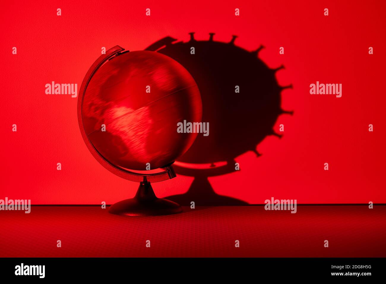 Globo que gira proyectando la sombra de células biológicas coronavirus en la pared roja Foto de stock