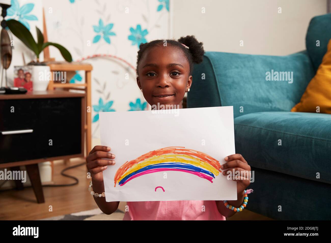 Retrato linda chica sosteniendo dibujo arcoiris en el salón Foto de stock