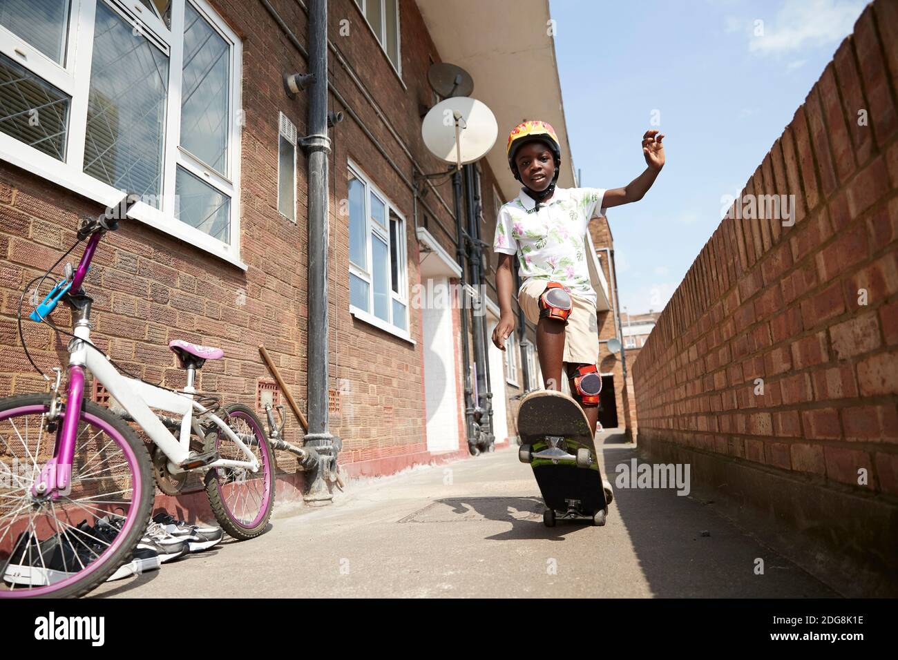 Retrato niño despreocupado skateboarding en el soleado callejón del apartamento Foto de stock