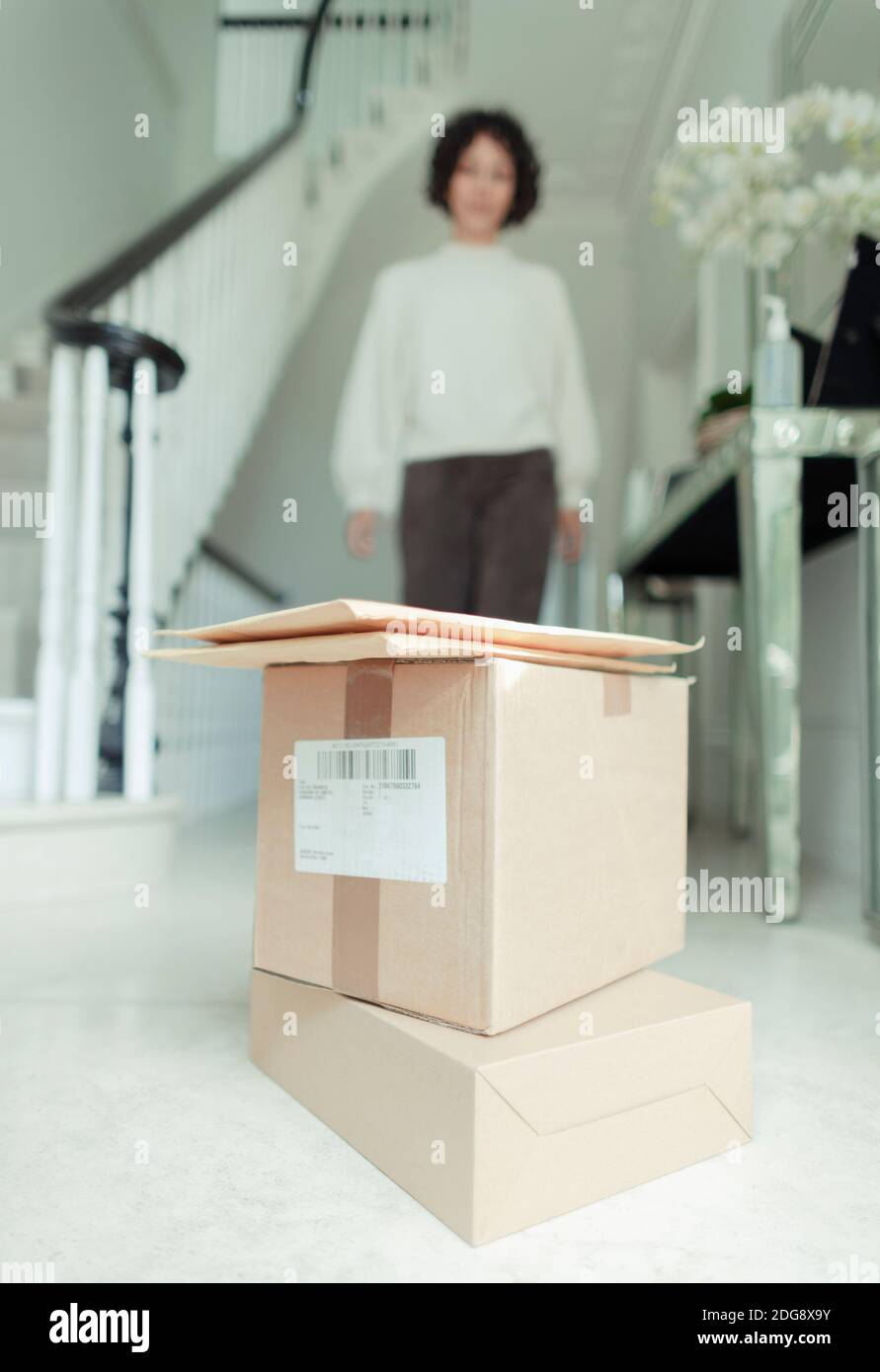 Mujer acercándose a la pila de cajas de entrega en el piso del vestíbulo Foto de stock