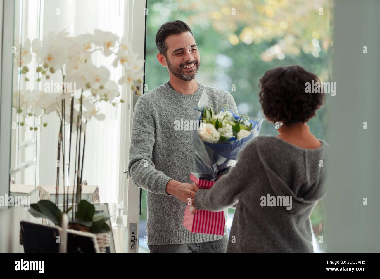 Marido feliz esposa sorprendente con flores en la puerta principal Foto de stock