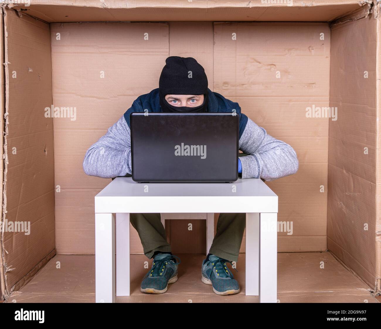 hacker cubre su cara mientras trabaja en un ordenador Foto de stock