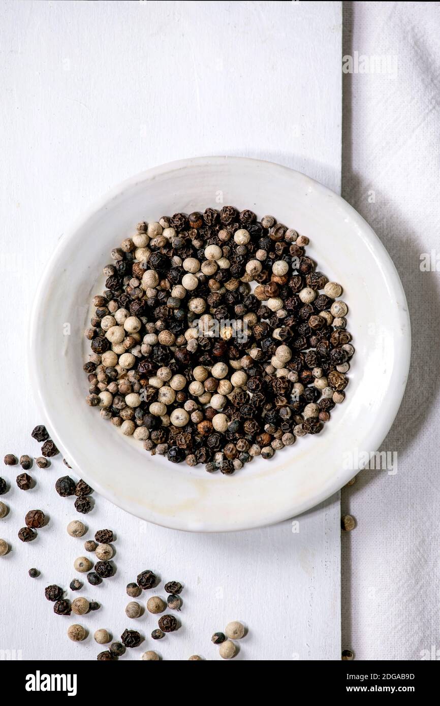 Mezcla de pimienta negra y blanca condimentando especias de pimienta en plato blanco sobre tabla de madera. Tela blanca como fondo. Plano, espacio Foto de stock