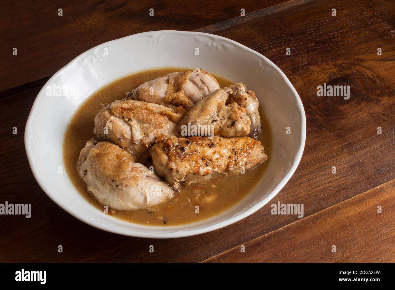 Vista superior de pollo cocido en salsa de verduras con coñac sobre plato blanco y una mesa de madera. Cocinar recetas en casa. Presentación de alimentos. Foto de stock