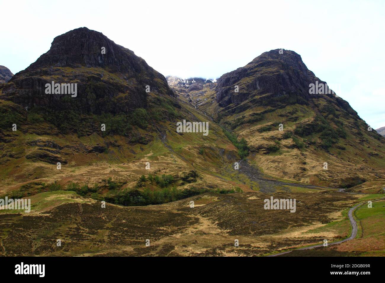 Un camino serpentea al pie de las montañas que dominan el valle de Glen Coe en la región de las tierras altas (Lochaber Geopark, Escocia) Foto de stock