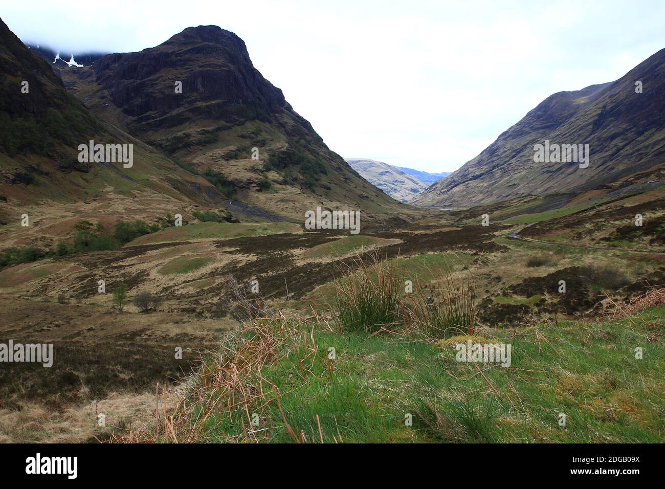 Algunos grupos de hierba cubren el pie de las montañas que dominan el valle de Glen Coe en las tierras altas (Lochaber Geopark, Escocia) Foto de stock