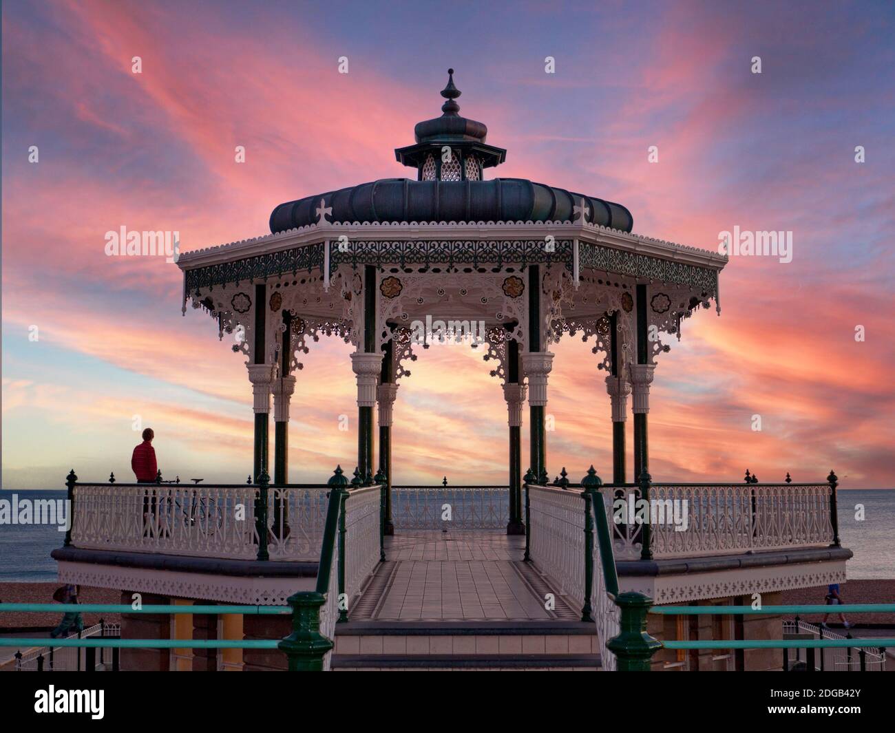 BRIGHTON Victorian Bandstand en el paseo marítimo a una puesta de sol roja Con una figura solitaria disfrutando de la vista panorámica del paisaje marino Brighton Sussex Reino Unido Foto de stock