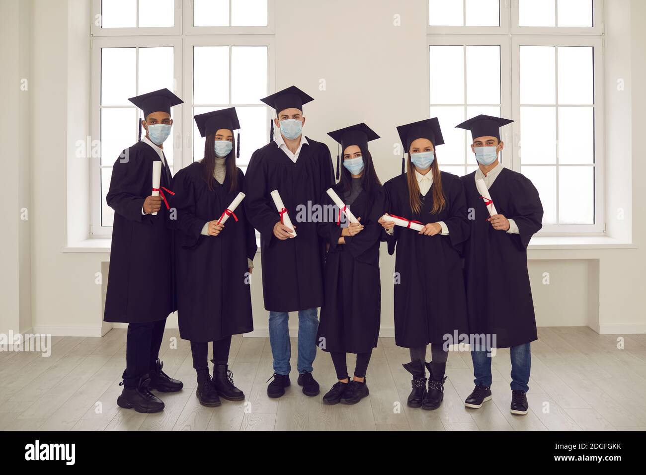 Retrato de estudiantes exitosos con diplomas en sus manos y con máscaras médicas en sus caras. Foto de stock