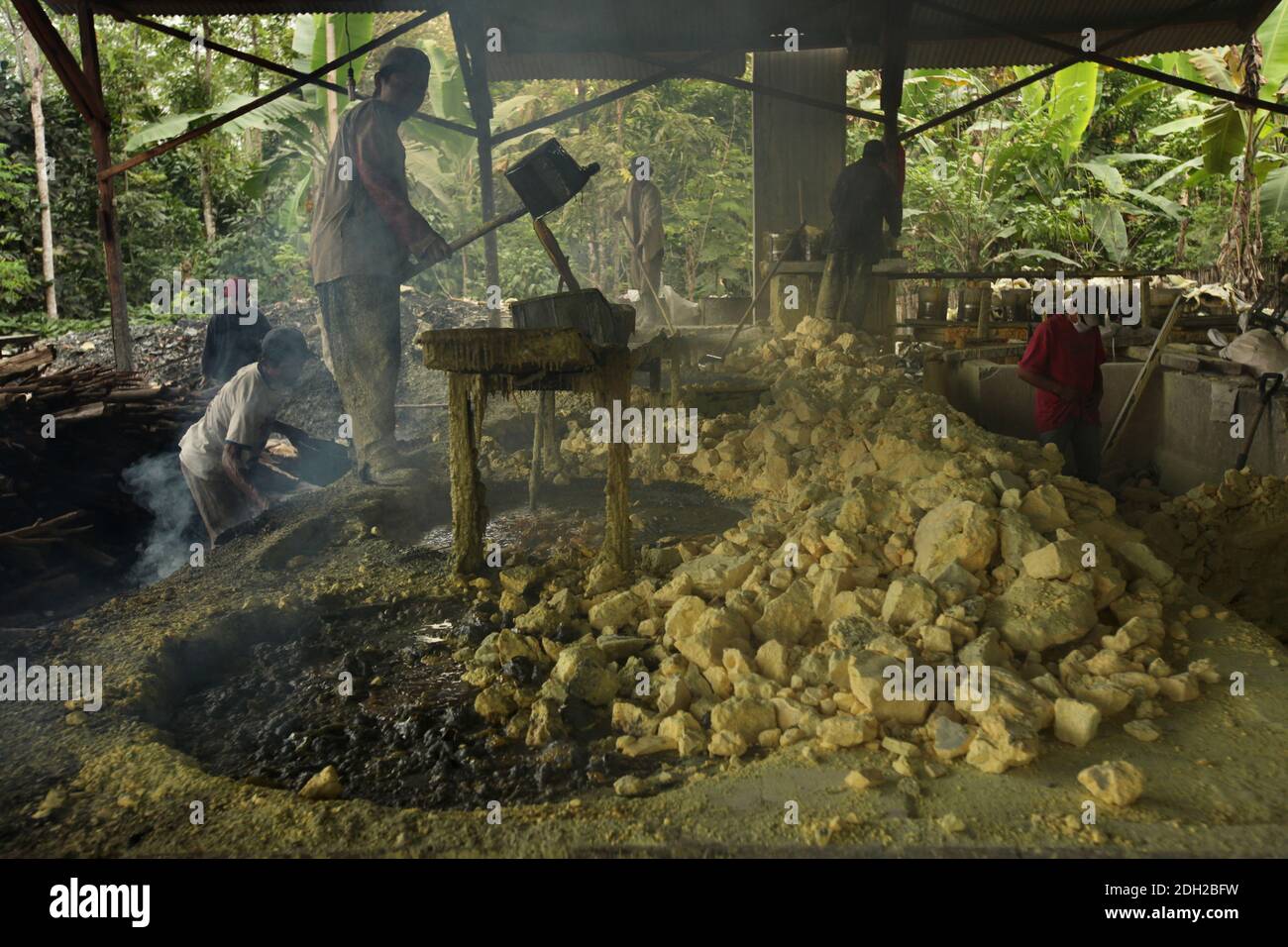 El trabajador de la fábrica carga el sistema de filtración con azufre fundido en humos tóxicos tóxicos tóxicos tóxicos venenosos en la fábrica de azufre de la aldea de Tamansari, en Java Oriental, Indonesia. La fábrica situada en la selva junto al pueblo procesa de 9 a 12 toneladas de azufre por día, entregadas aquí desde las minas de azufre cercanas en el cráter del volcán activo de Kawah Ijen. El azufre se funde en la fábrica, luego se filtra y se carga en sacos. Los trabajadores trabajan aquí en humos tóxicos venenosos. Se cree que el trabajo en la fábrica es aún más peligroso, que el trabajo en las minas de azufre. Foto de stock