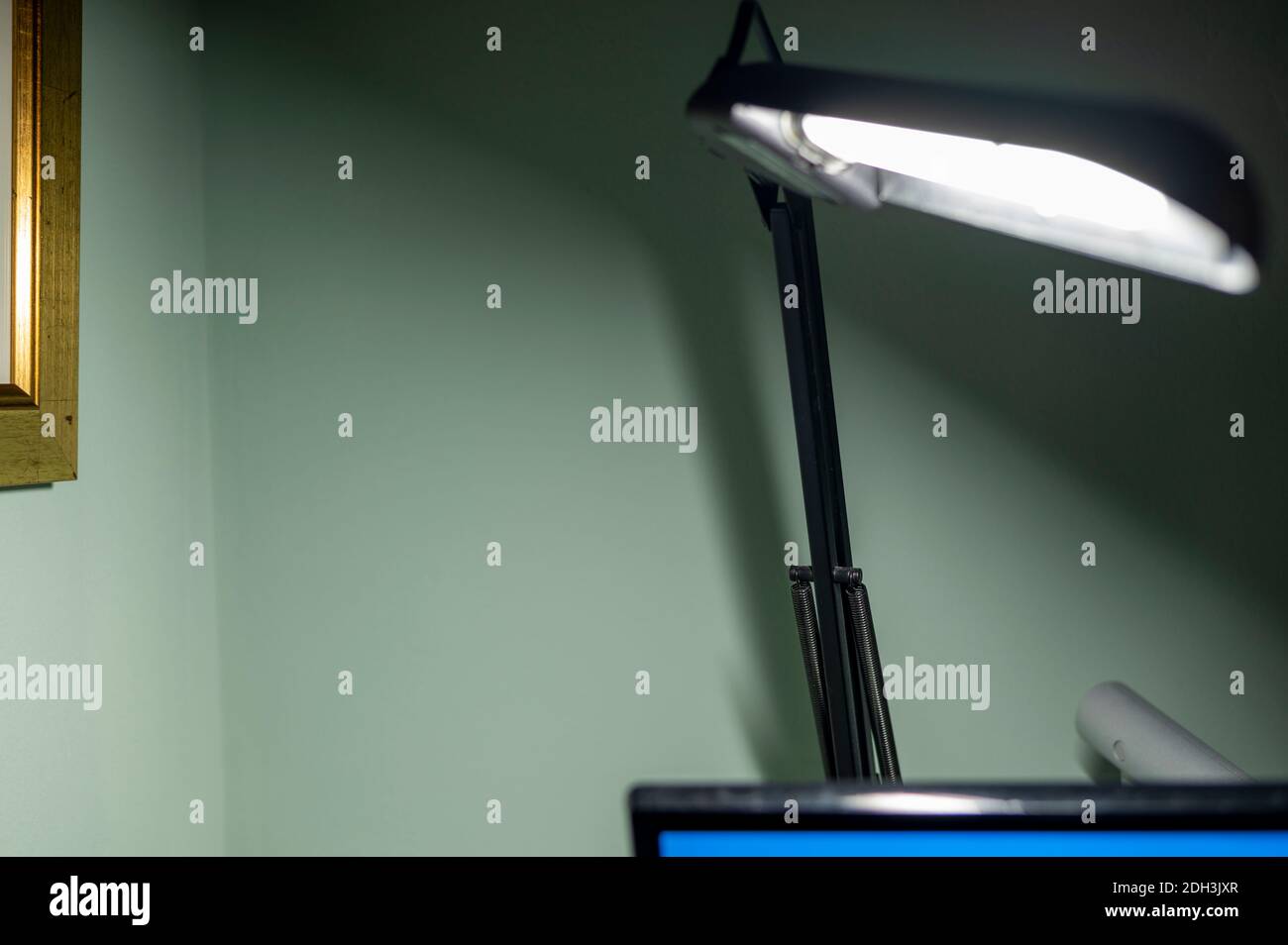 Lámpara de escritorio articulada con brazos negros en primer plano difuminada y con bombilla iluminada con su sombra en la pared. Foto de stock