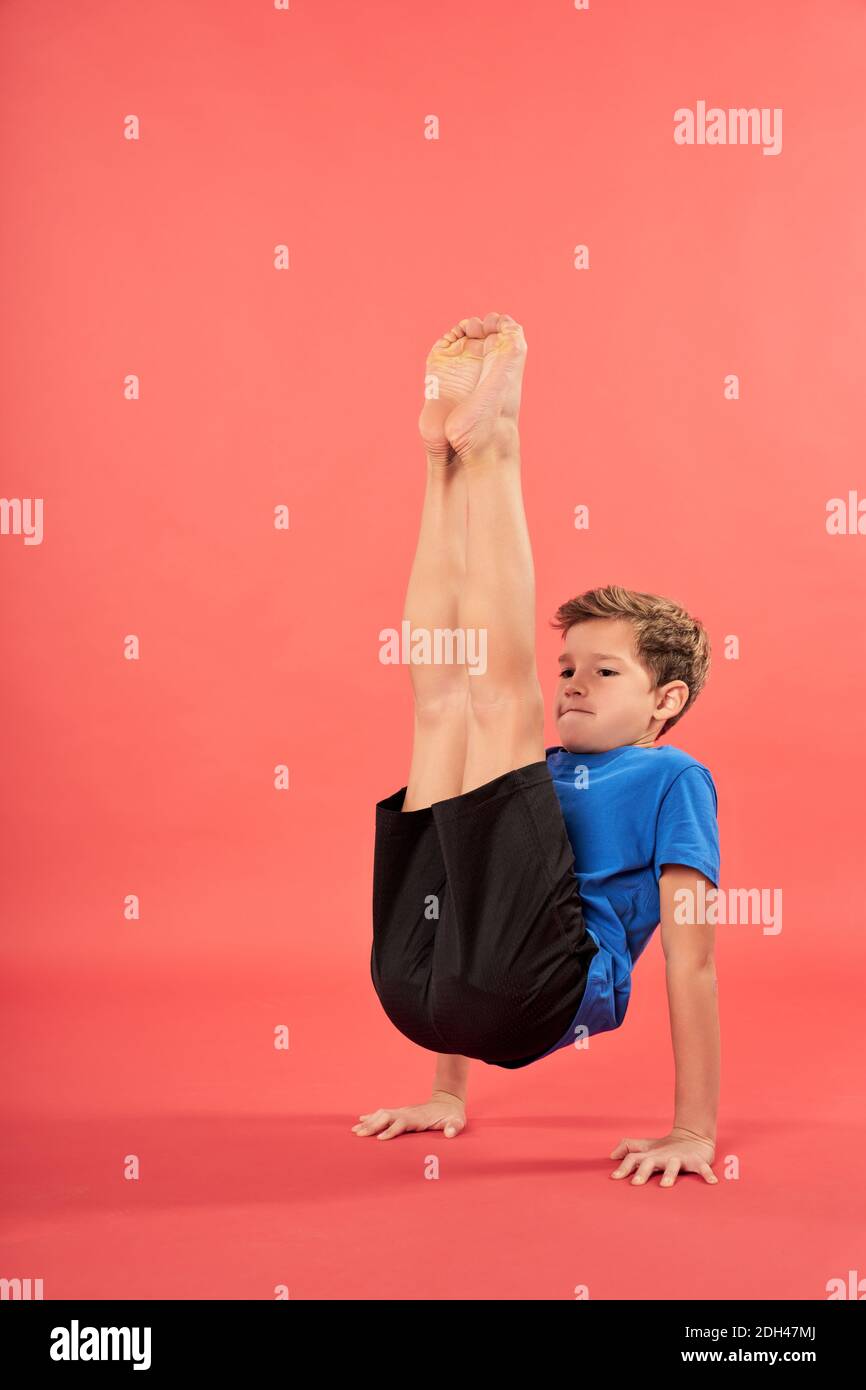 Lindo niño masculino en el equilibrio de ropa deportiva en dos manos y.. levantar las piernas mientras practica yoga Foto de stock