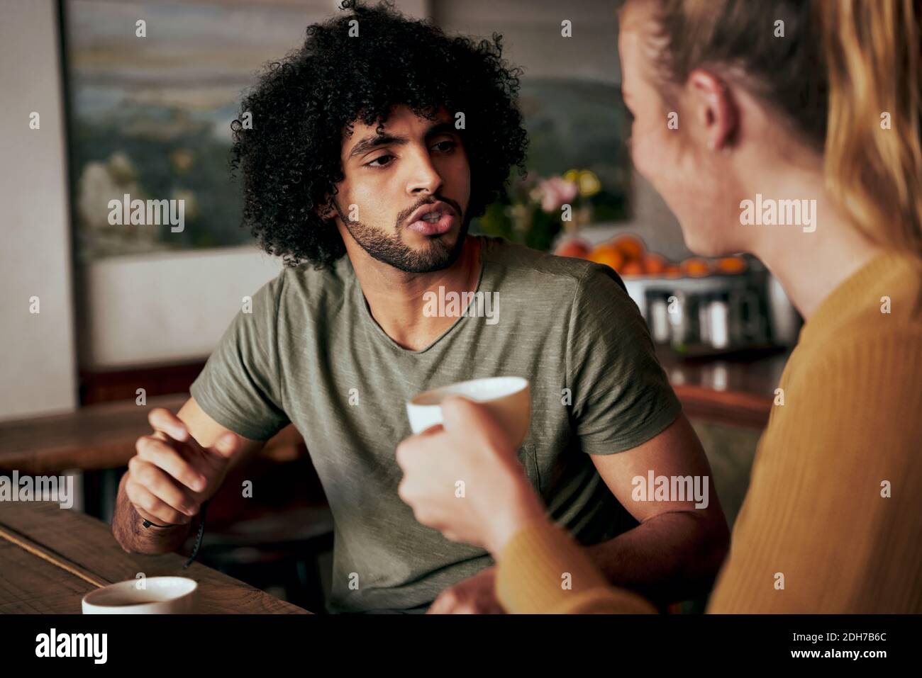 Joven afroamericano con un afro en una conversación seria con la mujer mientras estaba sentado en un café y bebiendo café - dos amigos diversos charlando Foto de stock