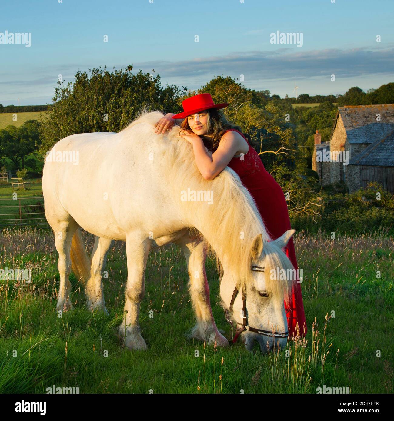 Una hermosa adolescente con un vestido rojo con un caballo blanco Foto de stock