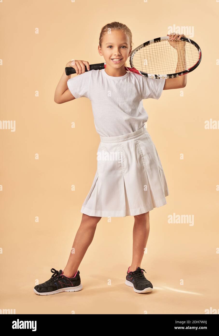 Adorable niña en uniforme de tenis mirando la cámara y.. sonriendo mientras  sostenía la raqueta de tenis Fotografía de stock - Alamy