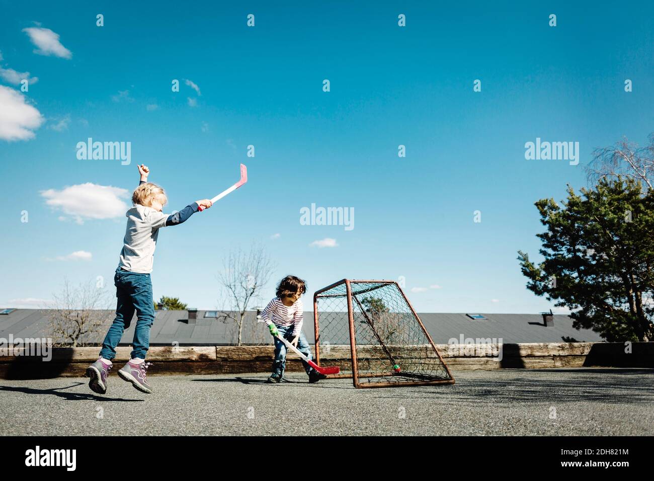 Emocionada chica jugando hockey con el niño en el patio contra el azul cielo Foto de stock