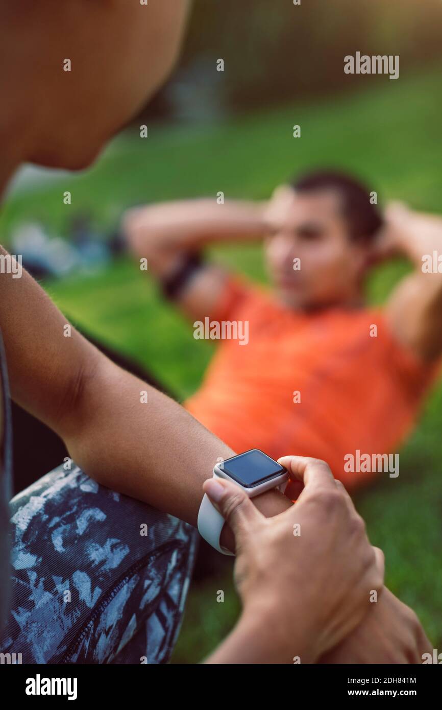 Mujer tocando el reloj inteligente mientras el hombre se sienta parque Foto de stock