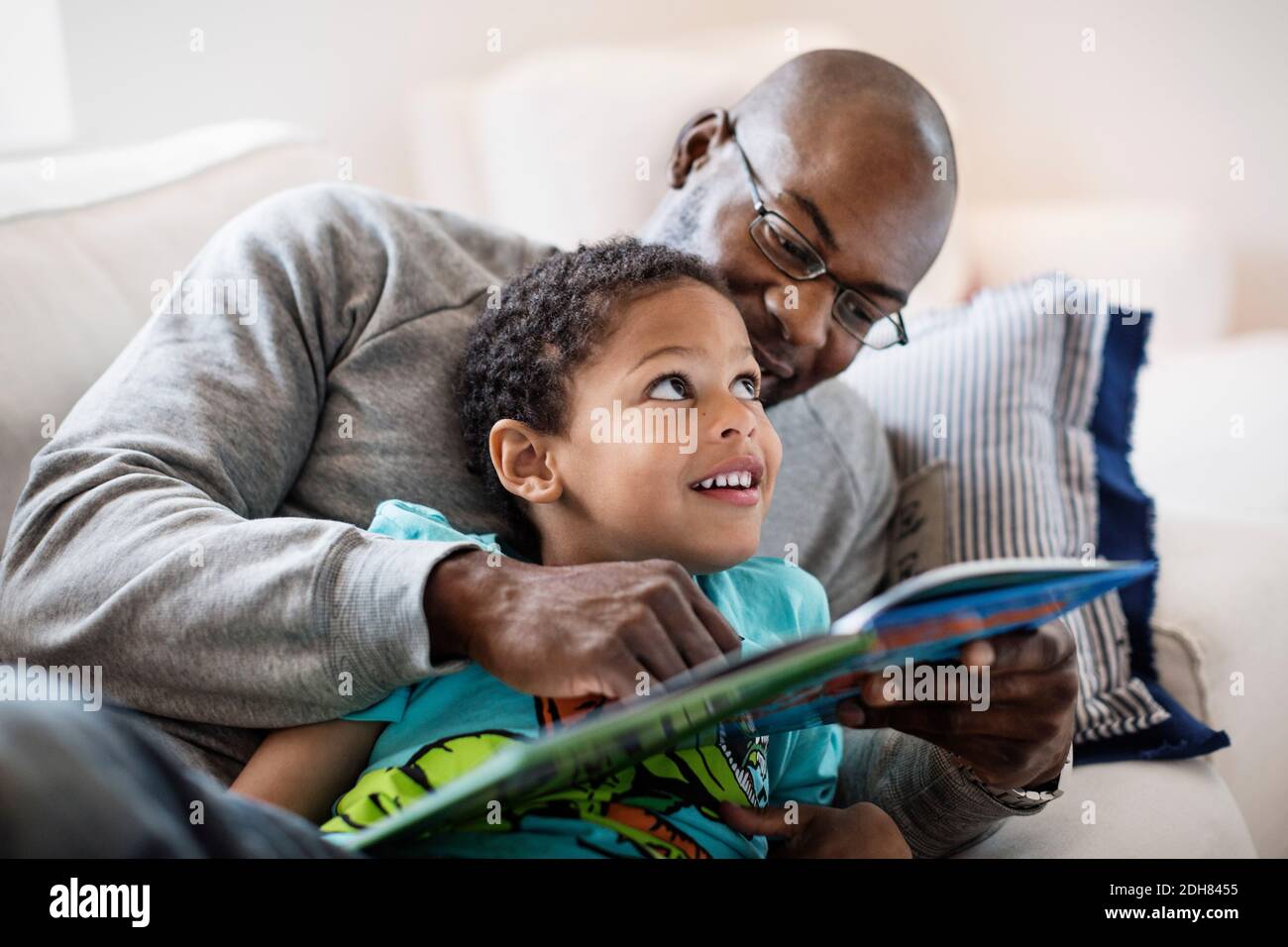 Niño sonriente mirando al padre mientras leía un libro de fotos inicio Foto de stock