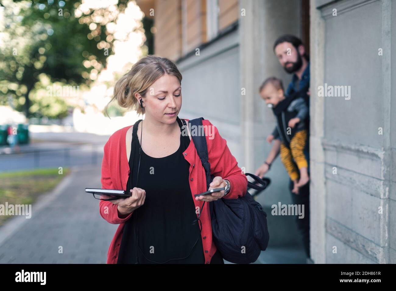 Mujer adulta mediana que usa el teléfono móvil mientras se va al trabajo con la familia en el fondo Foto de stock
