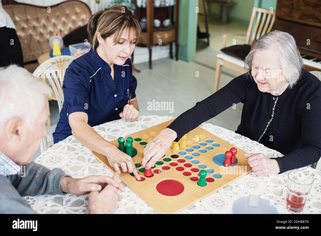 Cuidador jugando Ludo con ancianos en el hogar de ancianos Foto de stock