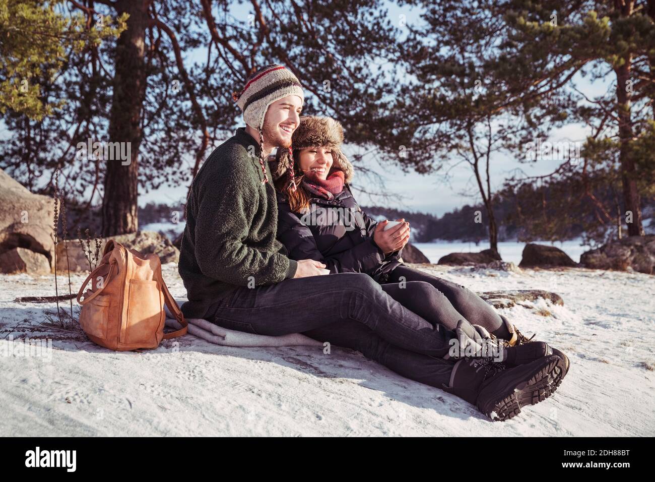 Feliz pareja disfrutando del café mientras se relaja en el campo cubierto de nieve Foto de stock