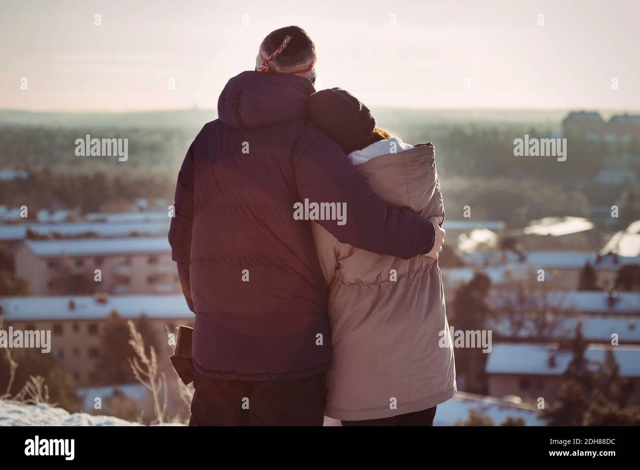 Vista trasera de la pareja abrazando mientras se está de pie en la montaña durante invierno Foto de stock