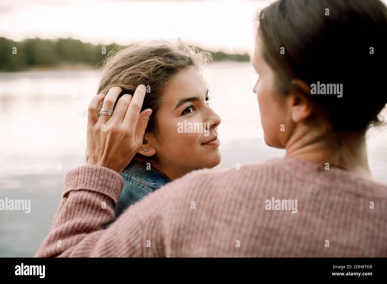 Una hija sonriente mirando a una madre cariñosa junto al lago Foto de stock