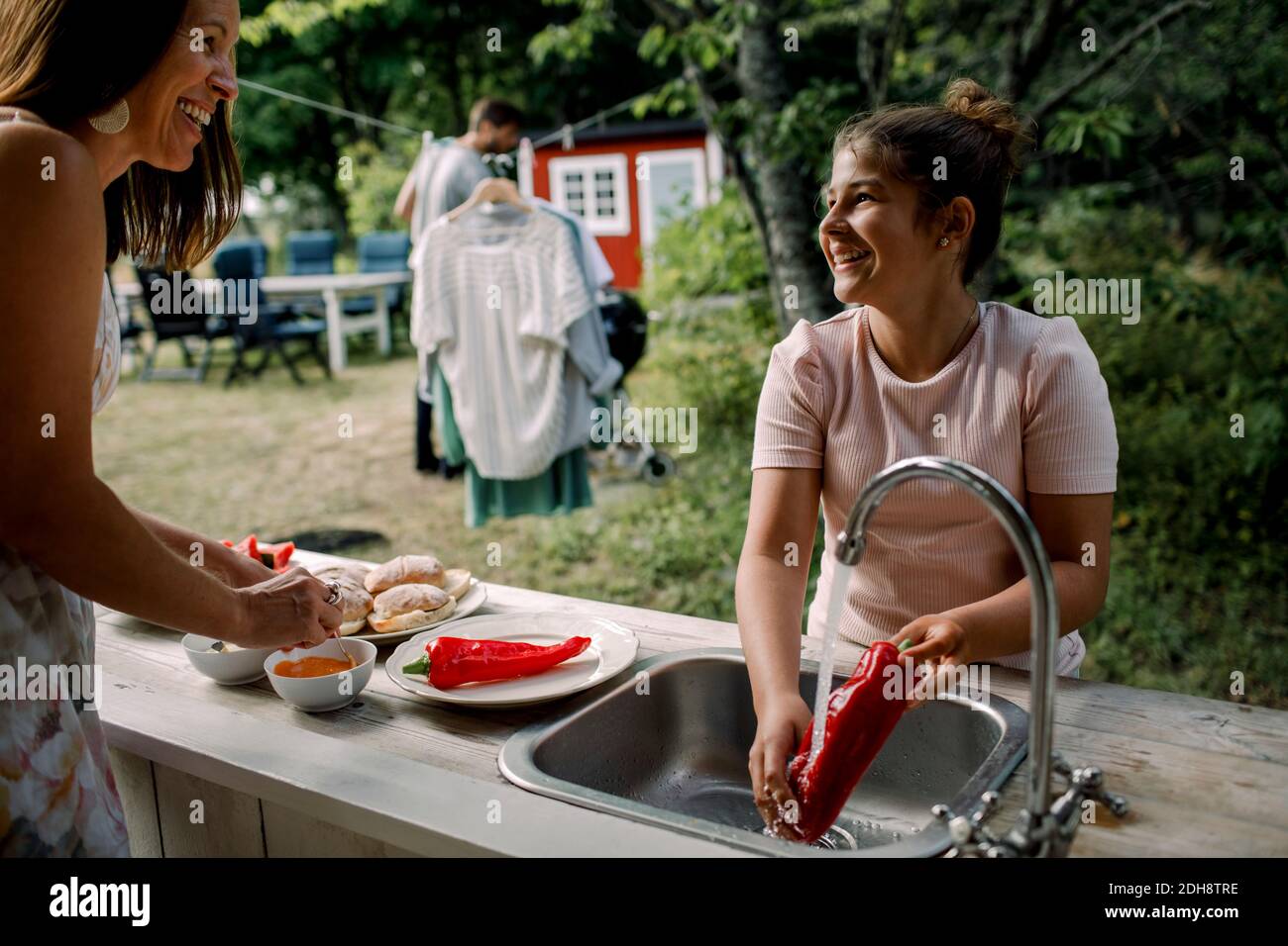 Sonriendo hija y madre hablando mientras preparan comida en el patio durante el verano Foto de stock